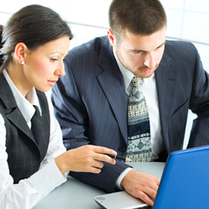 two people looking at a computer screen, where it appears as if one is instructing the other